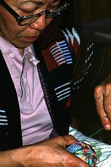 Un homme brode une balle de fils colorés formant un motif d’étoile.