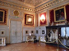 Angle d'une salle décorée de boiseries blanches, de tableaux en hauteur et comprenant une grande vitrine à droite