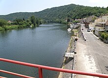 La photo couleur montre un mur maçonné qui surplombe la rivière. Une allée bâtie descend en pente douce jusque dans l'eau.