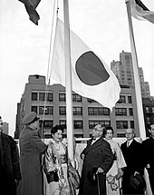 Um grupo de homens e mulheres assistindo ao hasteamento de uma bandeira.