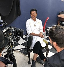 Woman in chef whites seated in front of microphones and cameras