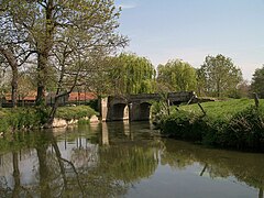 Photographie montrant un cours d'eau dans une lègère courbe à droite, avec un pont de pierres à trois arches en arrière-plan.