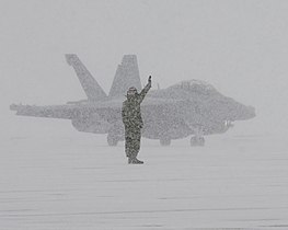 Sailor directing a fighter jet in a snowstorm