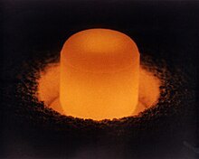 Glowing cylinder of plutonium oxide standing in a circular pit