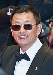 Wong Kar-wai at a film festival. He is wearing sunglasses and sports a buzzcut hairstyle in tuxedo and a bowtie