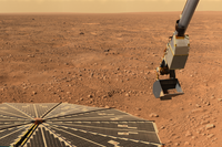 Zdjęcie. Skalista, rdzawa pustynia pod żółtawym niebem. Na pierwszym planie otwarty panel słoneczny i wysięgnik sondy.