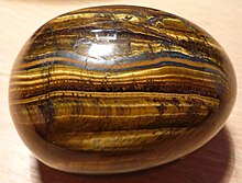"Photograph of a polished ovoid stone with bands containing shimmering golden fibers"