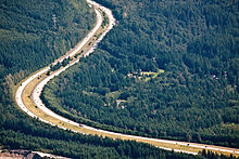 Aerial view of a divided highway making two turns in a densely forested area.