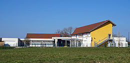 Un bâtiment à étage jaune et un bâtiment de plain-pied blanc encadrant une cours de récréation.