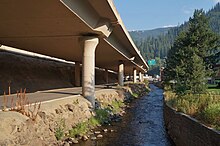 View underheath an elevated highway on the shores of a narrow river flanked by rocks and walls