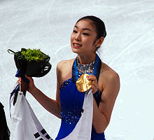 Photographie d'une femme en robe bleue, tête relevée, portant un drapeau blanc, dans sa main gauche une médaille d'or, dans sa main droite un bouquet de fleurs.