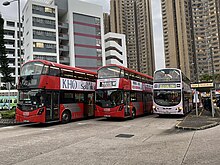 Three double-decker buses, two of them red, produced by Wrightbus at a bus stop in Hong Kong