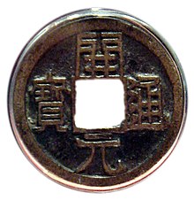 Fotografie v průhledném pouzdru, mince je kulatá s čtvercovým otvorem uprostřed a nápisem ze čtyř znaků čínského písma, vždy jeden znak podél každé strany otvoru, znaky jsou stejně veliké jako otvor a sahají až ke krajům mince