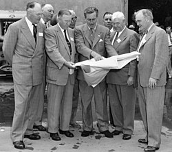 Photo noir et blanc d'un groupe d'hommes debout en costume qui se concentrent sur un plan