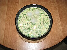 Mísa bílé polévky s velkým množstvím bylinek a třemi kostkami ledu