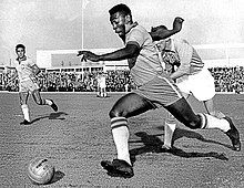 Photo noir et blanc d'un footballeur courant balle au pied devant deux adversaires au second plan