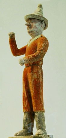 Fotografie keramické figurky (z podhledu) muže v červenooranžovém přiléhavém oděvu s vysokým špičatým kloboukem
