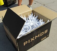 Box filled with white PixMob wristbands on a concrete surface, ready for distribution