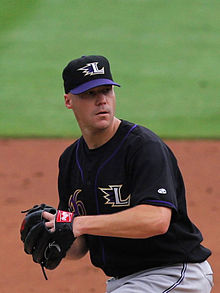 A baseball player wearing a black jersey and gray pants