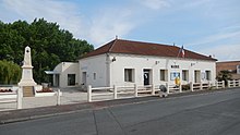 La mairie de Cabariot (un bâtiment blanc sans étage, assez simple), avec, à sa gauche, le monument aux morts de la commune.