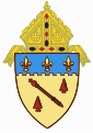 The arms of the Diocese of Baton Rouge: The shield features a red baton, referencing the city name, Baton Rouge, Louisiana, and its literal French meaning.