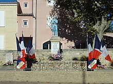 Une statue de Poilu peinte monte la garde sur un socle carré. Monument pavoisé pour le 11 novembre
