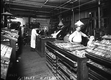 Photographie en noir et blanc d'ouvriers travaillant à la création d'un journal papier au début du XXe siècle.