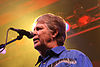 A man with graying hair behind a microphone, wearing a blue dress shirt with music notes and piano keys.