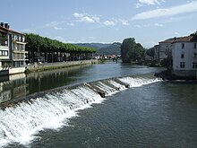 Photographie couleur du cours d'une rivière obstruée par une chaussée de un à deux mètres de hauteur.