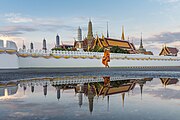 Monk walks in the morning after the rain in front of the Temple of the Emerald Buddha (Wat Phra Kaew), part of the Grand Palace, Bangkok, Thailand.