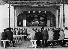 Soldiers and other sitting on benches in front of a stage