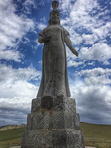 A large stone statue, atop a podium, of a robed woman with an elaborate headdress