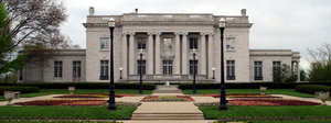 A two-story stone mansion with a sprawling flower garden in front