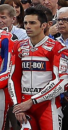 Dark haired motorcycle rider in leather racewear standing as part of a startline gathering prior to a race