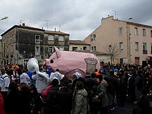 Une foule promenant un gros cochon rose en carton pâte lors d'un carnaval à Poussan