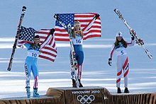 Photographie de trois skieuses sur un podium, deux d'entre elles brandissant le drapeau des États-Unis, l'autre portant ses skis.