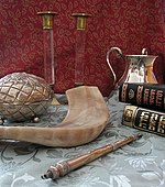 Photo représentant divers accessoires pour les temps fixés du judaïsme disposés sur une table : les chandeliers de chabbat, le keli (à l'arrière-plan), le Houmash, le Tanakh, le pointeur de lecture, le chofar et la boîte pour etrog.