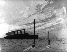 A black-and-white film still. An ocean scene. In the distance is an ocean liner. In the foreground, two periscopes breach the water.