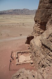 Foundations of a small stone wall at the base of a desert cliff