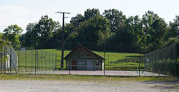 Cabane et cours de tennis entourés d'un haut grillage.