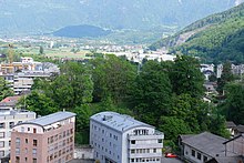 Colline verte avec des arbres au sommet, au milieu de bâtiments.