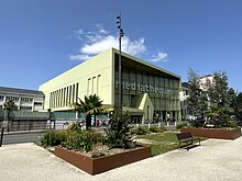 Photographie en couleurs d'un bâtiment vert avec façade vitrée.