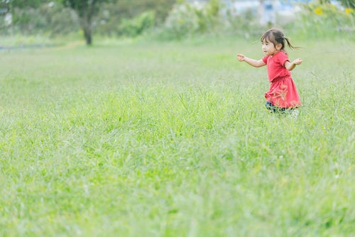 原っぱを無邪気に走り回る小さい女の子の写真