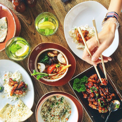 A hand holding chopsticks reaches in to take food from one of several plates of delicious-looking food.