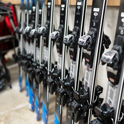 A collection of grey and blue skis line up against the Gear Garage wall.