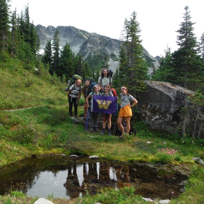 First Year Adventures participants hold up a UW purple flag in a beautiful mountain setting.