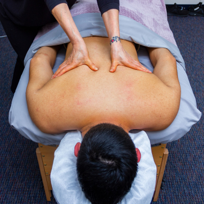 The Massage Clinic logo depicting a graphic of a masseuse giving a massage to an individual in a purple and white color scheme.