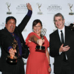 Three people holding Emmy awards and celebrating.