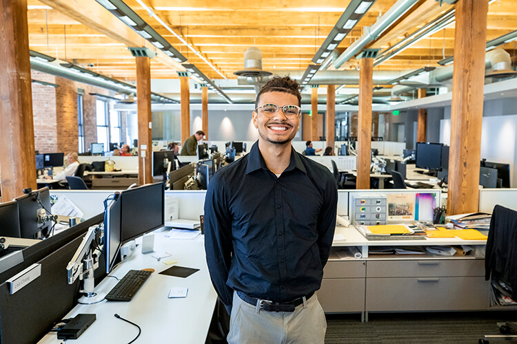 Young man standing in an office setting with cubicles and computers