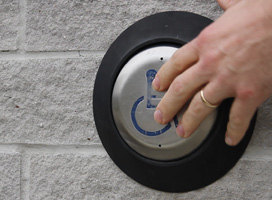 A hand pressing the door opener for an accessibility entrance.